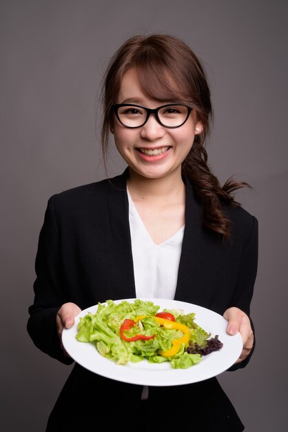 Feliz empresaria asiática sosteniendo ensalada mientras sonríe