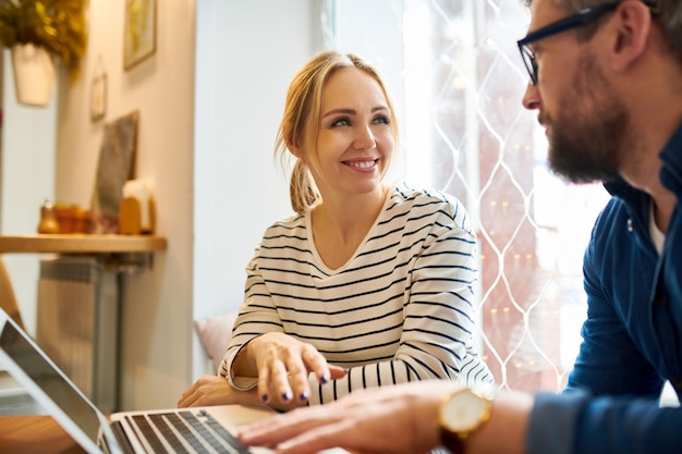 Feliz empresaria casual rubia joven mirando a su colega en la reunión de trabajo durante la discusión de datos