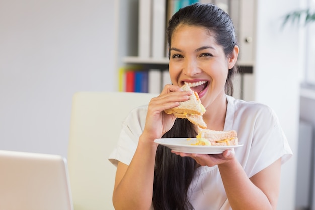 Feliz empresaria comiendo sandwich