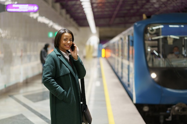 Feliz empresaria exitosa regresar a casa del trabajo hablar por teléfono esperar el tren en la plataforma del metro