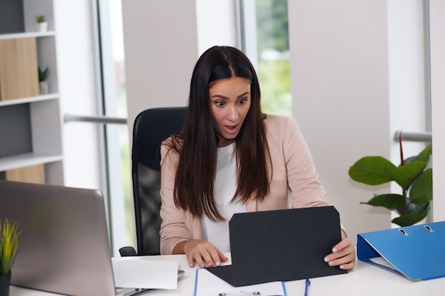 Feliz empresaria con gesto de la mano levantada leyendo la carta en el escritorio frente a la computadora portátil. El empresario está satisfecho con las buenas noticias de la correspondencia.