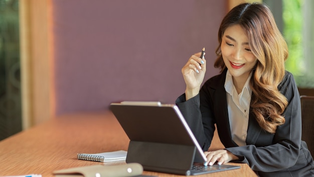 Feliz empresaria joven empresaria trabajando en tableta, mantenga lápiz en la oficina