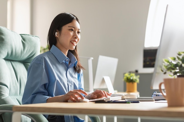 Feliz empresaria milenaria asiática trabajando en línea en la computadora en la oficina