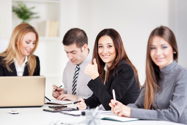 Feliz empresária mostrando os polegares no escritório. Olhando para a câmera.