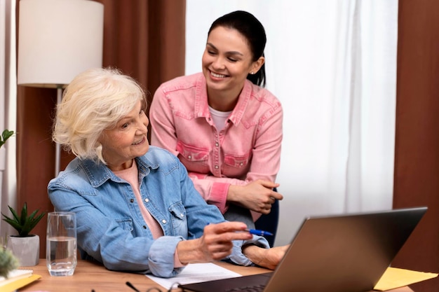 Feliz empresária sênior apontando a tela do laptop enquanto trabalhava em casa Filha sorridente parada por perto com emoções de prazer Bela senhora idosa elegante navegando no site no computador