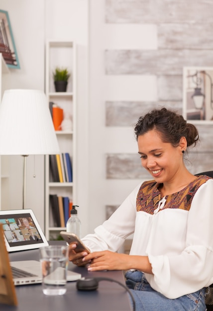 Feliz empresaria con smartphone mientras trabaja desde casa.