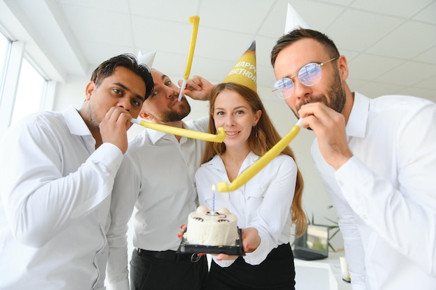 Feliz empresaria sosteniendo pastel de cumpleaños mientras hacía una fiesta sorpresa con sus colegas en la oficina