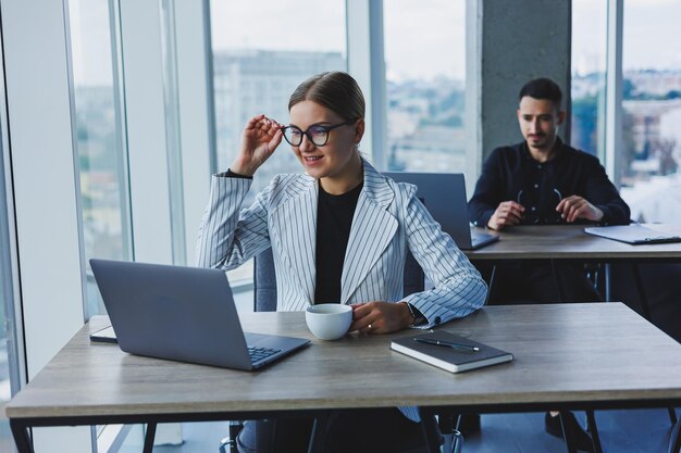 Feliz empresária trabalhando no laptop conceito de cooperação empresarial e trabalho em equipe jovens à mesa no escritório pessoas modernas de sucesso