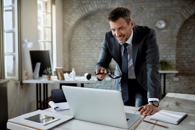 Feliz empresário adulto médio lendo um e-mail no laptop enquanto trabalhava no escritório