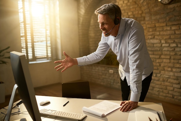 Feliz empresário adulto médio usando computador e fazendo videochamada enquanto trabalhava no escritório