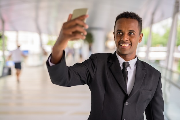 Feliz empresario africano tomando selfie mediante teléfono móvil al aire libre