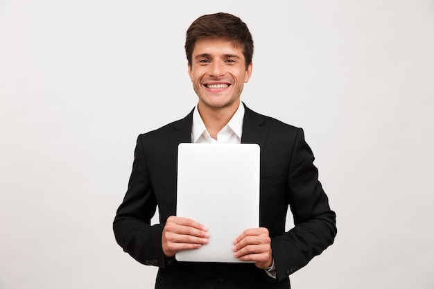 Feliz empresário alegre em pé isolado segurando o computador portátil.