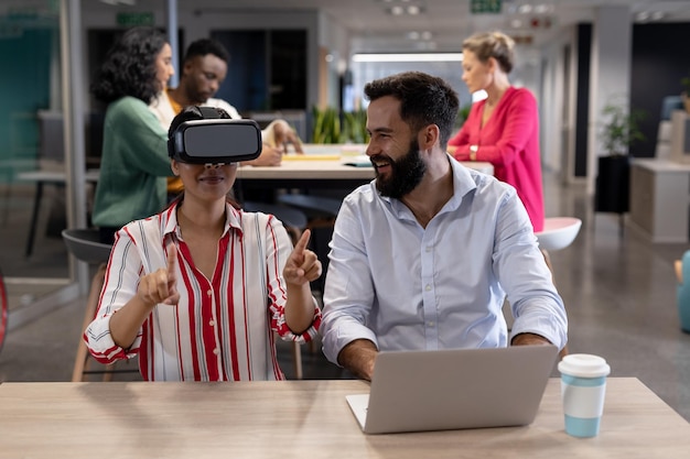 Feliz empresário caucasiano olhando empresária birracial gesticulando enquanto experimenta fone de ouvido vr