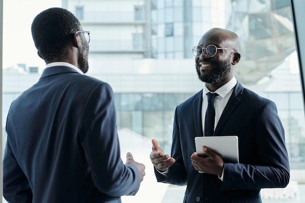 Feliz empresário com tablet conversando com colega do sexo masculino na reunião de trabalho