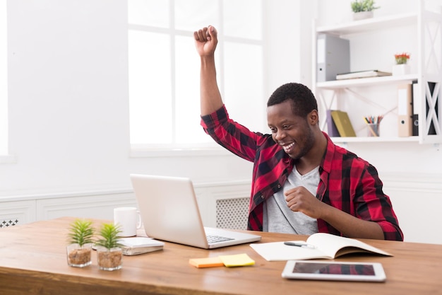 Feliz empresário comemorar, vencer. Vencedor, homem negro casual no escritório com laptop