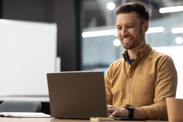 Feliz empresário digitando usando laptop sentado no local de trabalho no escritório