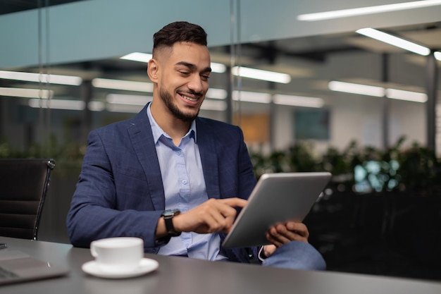Foto feliz empresário do oriente médio trabalhando no escritório usando tablet digital