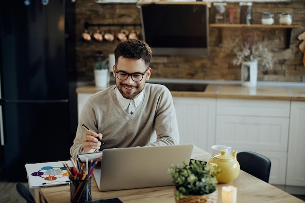 Feliz empresário escrevendo notas enquanto trabalhava no laptop em casa