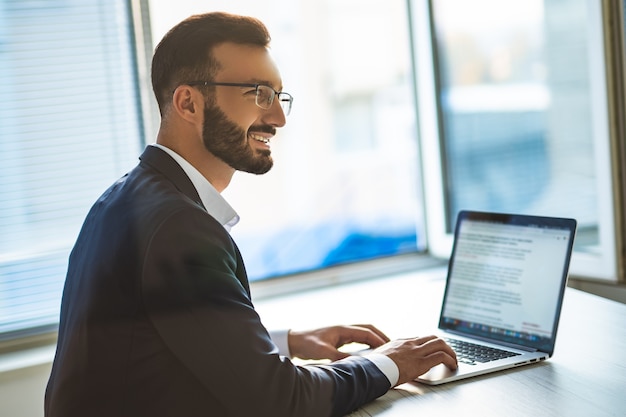 El feliz empresario de gafas trabajando con un ordenador portátil en la mesa