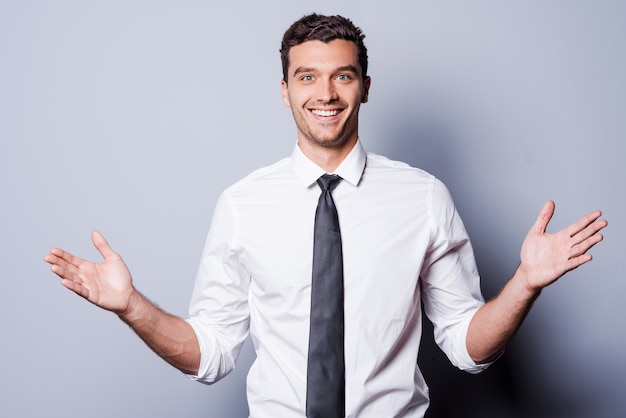 Feliz empresário gesticulando. Jovem feliz de camisa e gravata gesticulando e sorrindo em pé contra um fundo cinza