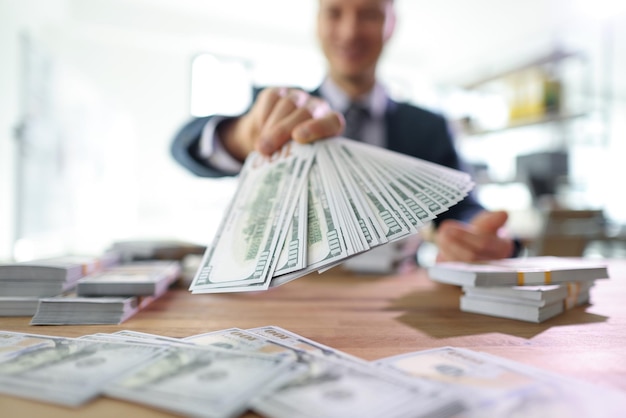 Foto feliz empresário mantém ventilador de notas de dinheiro acima de notas de dólar espalhadas na mesa com sucesso