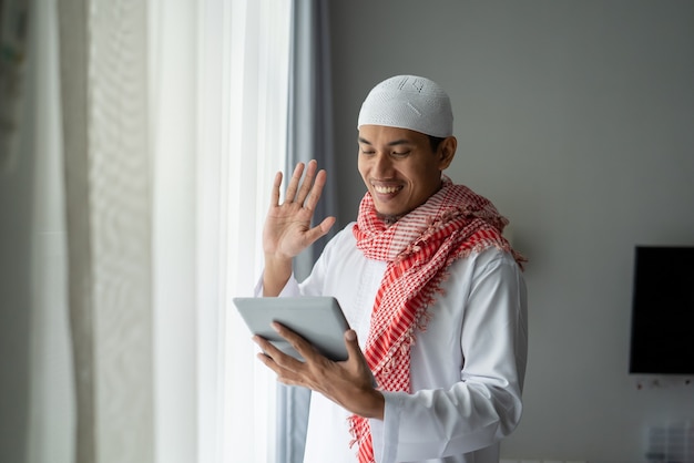 Feliz empresario musulmán sonriendo mientras usa tablet pc cerca de la ventana