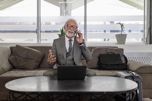 Feliz empresário ou empresário falando no telefone inteligente enquanto estiver usando o laptop no salão do hotel