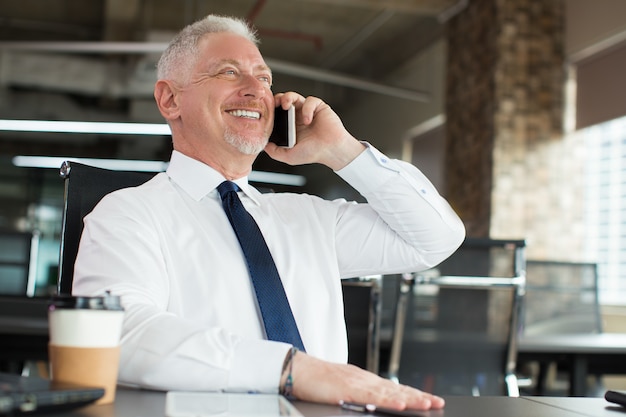 Feliz empresário sênior bem sucedido usando o telefone