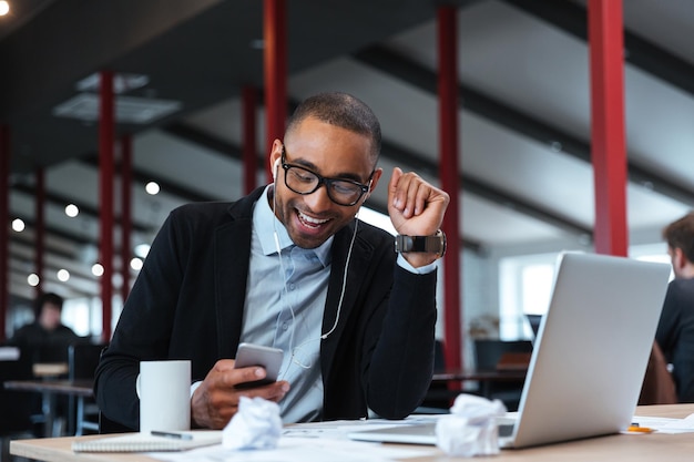 Feliz empresário sorrindo e mandando mensagens de texto no smartphone na mesa