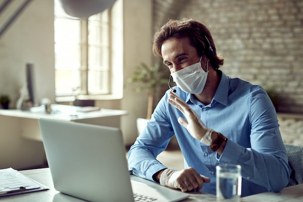 Feliz empresário tendo chamada de vídeo enquanto trabalhava no escritório durante a epidemia de coronavírus