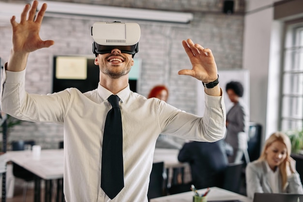 Feliz empresário testando fone de ouvido de realidade virtual e se divertindo no escritório Há pessoas em segundo plano