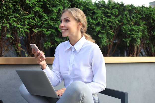 Feliz empresario trabajando con un teléfono y una computadora portátil cerca de la oficina.