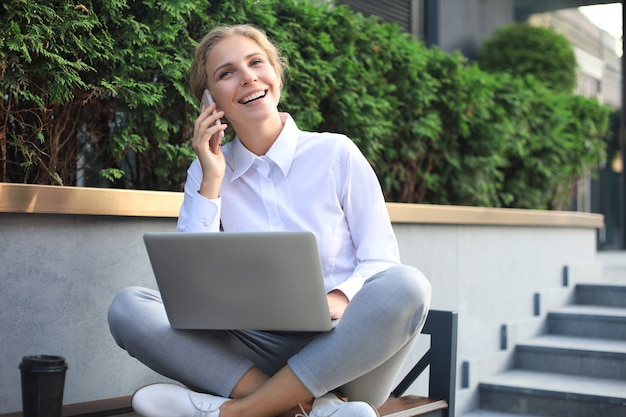 Feliz empresário trabalhando com um telefone e um laptop perto do escritório.