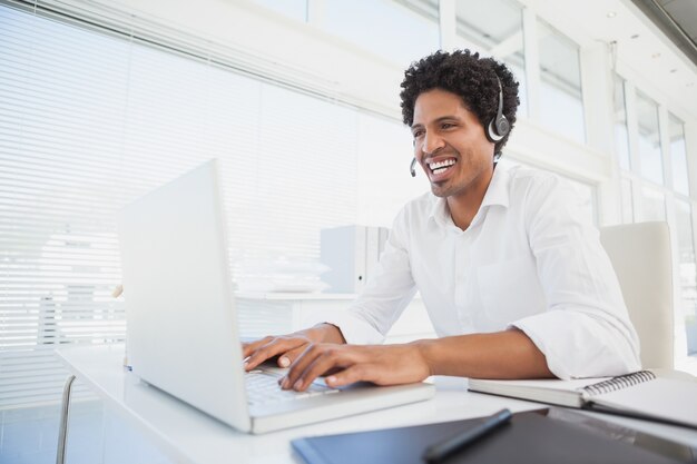 Feliz empresário trabalhando em sua mesa com fone de ouvido