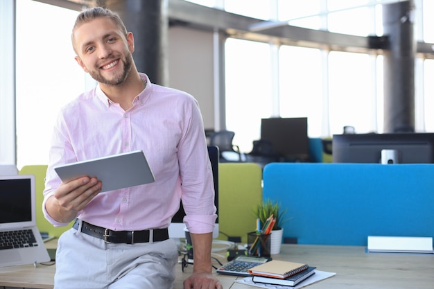 Feliz empresário trabalhando usando tablet digital enquanto está sentado no escritório.