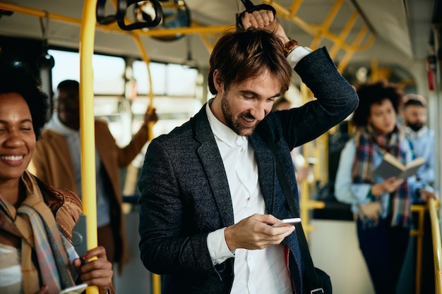Feliz empresário usando telefone inteligente enquanto viaja para o trabalho de ônibus
