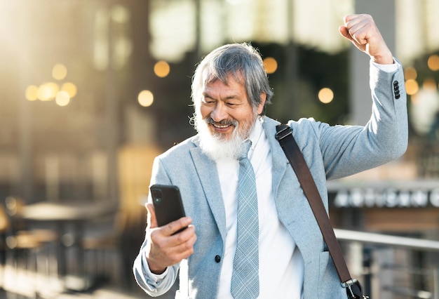 Feliz empresário vencedor ou celebração por telefone para o sucesso da loteria negócio corporativo ou crescimento da empresa financeira na cidade Sorria bomba de punho ou uau homem sênior vencendo competição on-line no aplicativo para smartphone