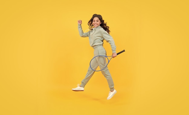 Feliz y enérgica jovencita salta en ropa deportiva con raqueta de bádminton corriendo hacia el éxito, date prisa