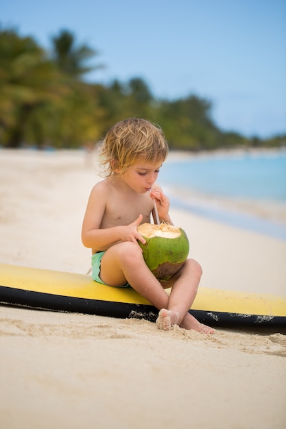 Feliz engraçado pré-escolar garoto menino bebendo suco de coco na praia do oceano.