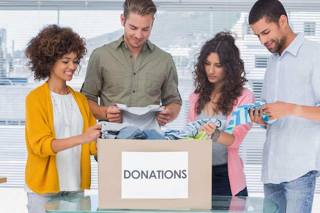 Foto feliz equipe de voluntários tirando roupas de uma caixa de doação