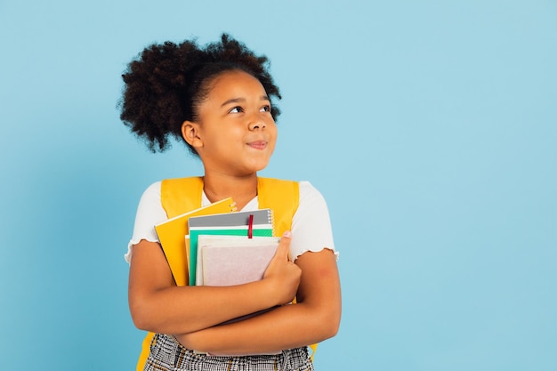 Feliz escolar afroamericana con libros en el fondo azul de vuelta al concepto de la escuela