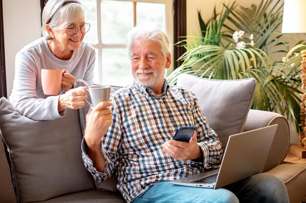 Feliz esposo y esposa de los años 70 descansan en el sofá en la sala de estar disfrutan del té hablando y relájate en el sofá