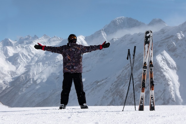 Feliz esquiador con esquís atascados en la nieve levante las manos sobre montañas nevadas