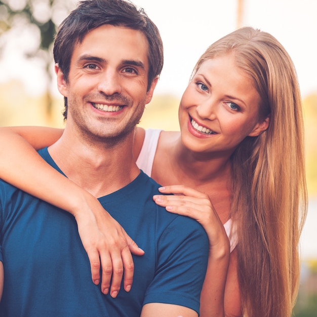 Feliz de estar juntos. Retrato de una hermosa joven pareja amorosa sonriendo y mirando a la cámara mientras está de pie al aire libre