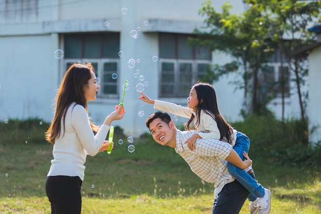 Feliz estilo de vida asiático madre familiar, padre y niña linda divirtiéndose juntos y disfrutando del juego al aire libre soplando burbujas de jabón en el parque del jardín en un día soleado, en verano