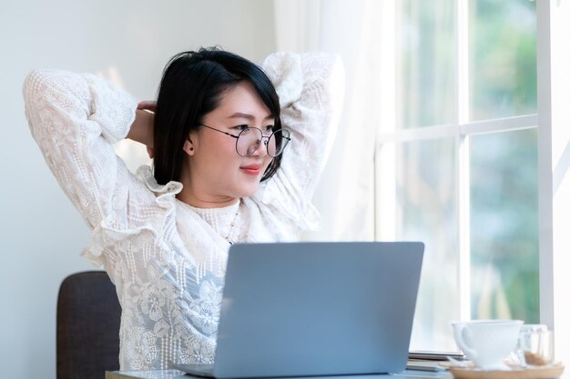 Feliz Estiramiento Relajación Descanso de personas independientes asiáticas mujeres de negocios informales que trabajan con una computadora portátil con una taza de café y un teléfono inteligente en una cafetería el concepto de comunicación de fondo