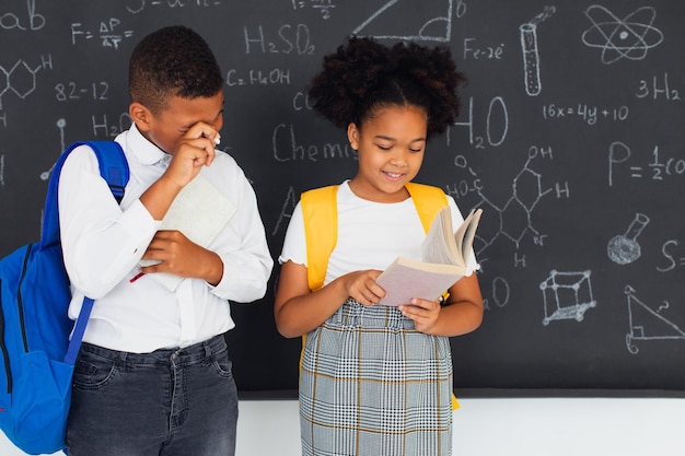 Feliz estudante afro-americana e estudante de raça mista resolvendo problemas perto do conselho escolar de volta ao conceito escolar