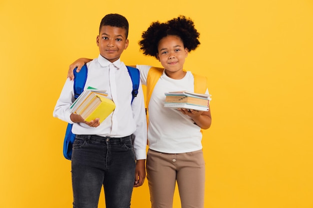 Feliz estudante afro-americana e estudante de raça mista segurando livros no espaço de cópia de fundo amarelo