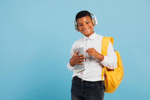 Feliz estudante de raça mista usando fones de ouvido e mochila segurando livros e cadernos de volta ao conceito de escola