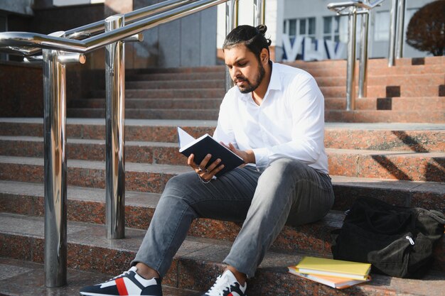 Feliz estudante indiano sentado nas escadas do campus universitário